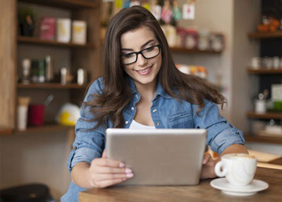 image of a person in glasses using their computer and drinking coffee